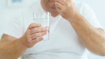 A man takes a pill with a glass of water