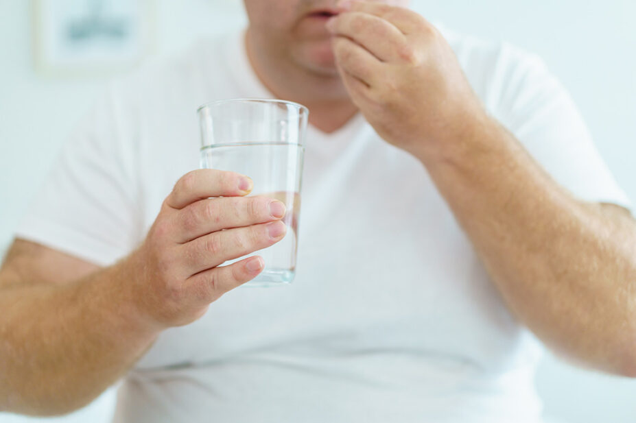 A man takes a pill with a glass of water