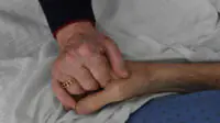 An older couple holds hands while husband is in palliative care