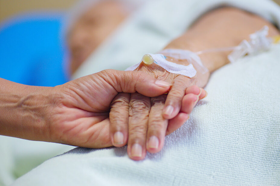 An older person with an IV holds a loved one's hand