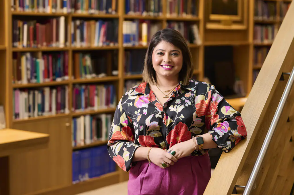 Amandeep smiles at the camera, wearing a floral shirt in a library