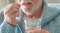 An older man takes a tablet with a glass of water