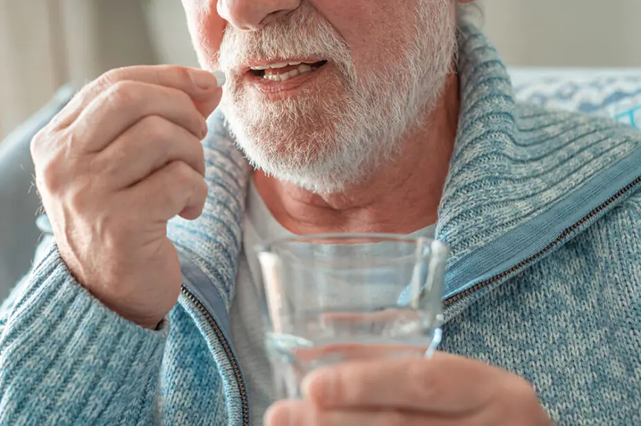 An older man takes a tablet with a glass of water