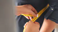 A clinician measuring a female's waist with a measuring tape