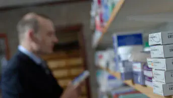 A pharmacist in the dispensary looking at medicine shelves