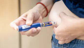 A person injects themselves in the stomach with an insulin pen