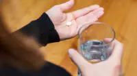 A woman takes a tablet with a glass of water