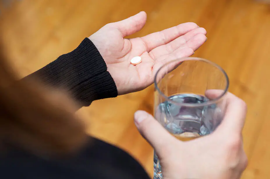 A woman takes a tablet with a glass of water