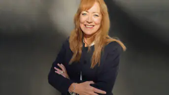 Catherine smiles with her arms crossed in front of her, grey background