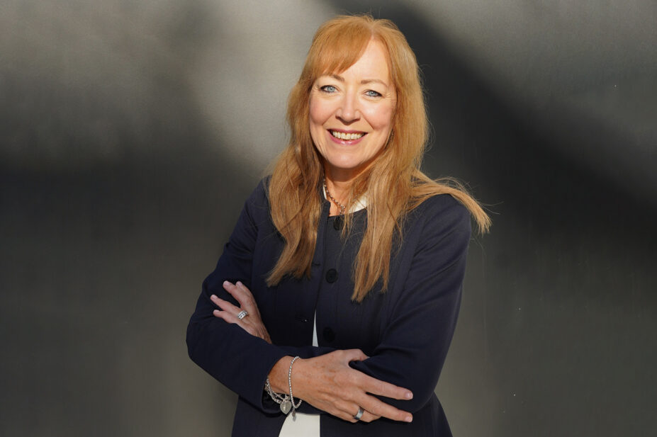 Catherine smiles with her arms crossed in front of her, grey background