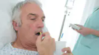 A older man takes a tablet while in a hospital bed