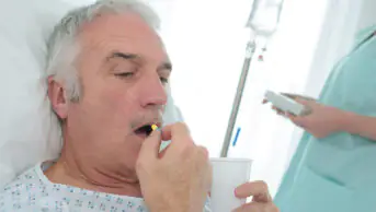 A older man takes a tablet while in a hospital bed