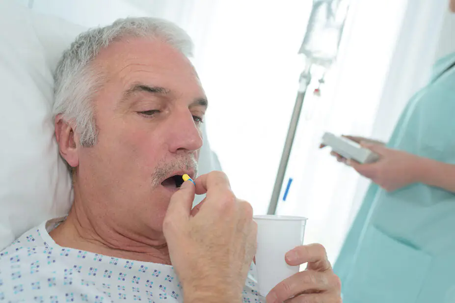 A older man takes a tablet while in a hospital bed