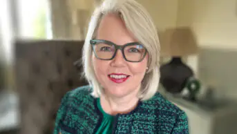 Justine smiles wearing glasses, her hair down and sitting in an office