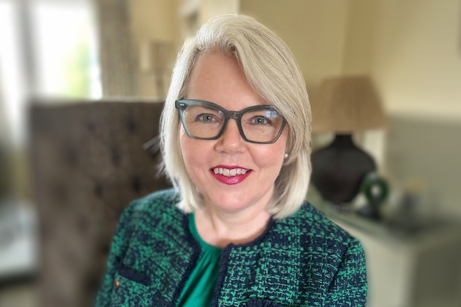 Justine smiles wearing glasses, her hair down and sitting in an office