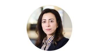 Round image of Amira looking serious in a shirt and blazer on a white background