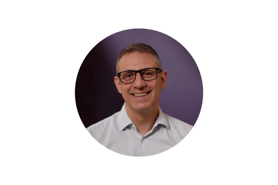 Mark smiling wearing glasses and shirt, on a purple background
