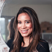 Melissa smiles in front of a mirror, with her hair down and wearing a black jacket