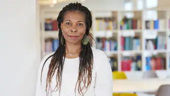 Portrait of Tase Oputu, standing in front of book shelves