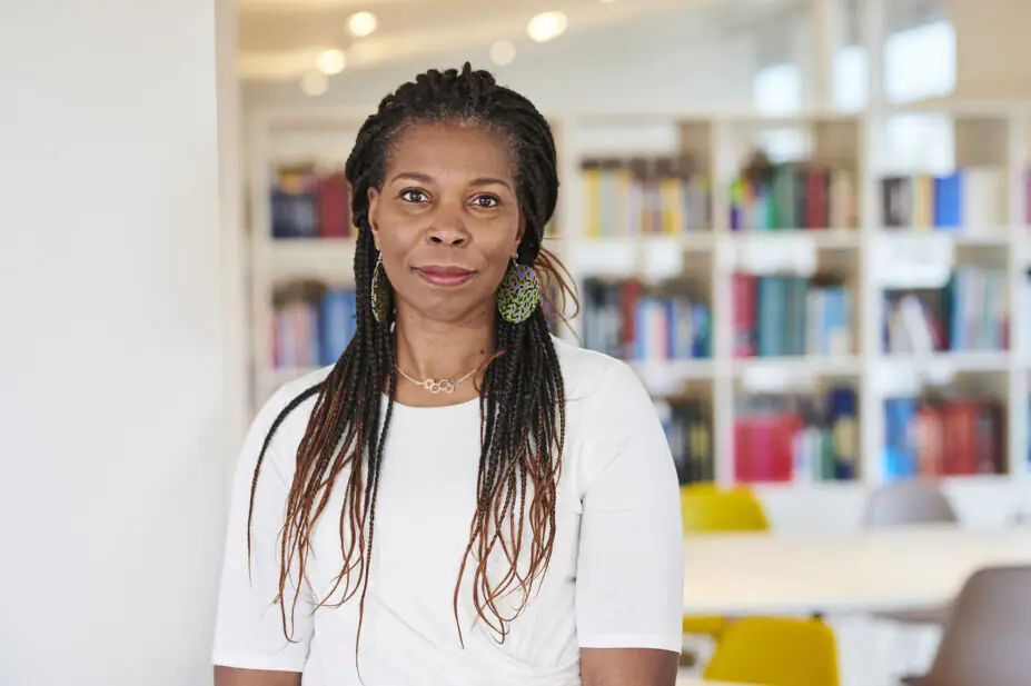 Portrait of Tase Oputu, standing in front of book shelves
