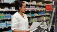A pharmacist works on the computer at the front desk of a community pharmacy
