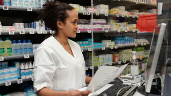 A pharmacist works on the computer at the front desk of a community pharmacy