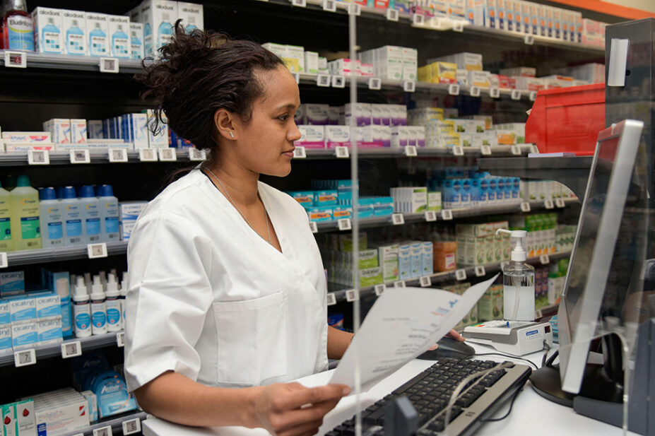A pharmacist works on the computer at the front desk of a community pharmacy