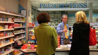 A pharmacist hands a prescription to a customer