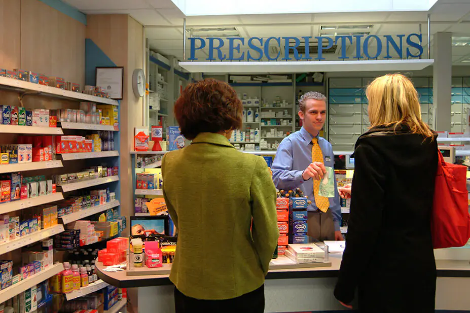 A pharmacist hands a prescription to a customer