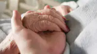 An older person with an IV holds a loved one's hand