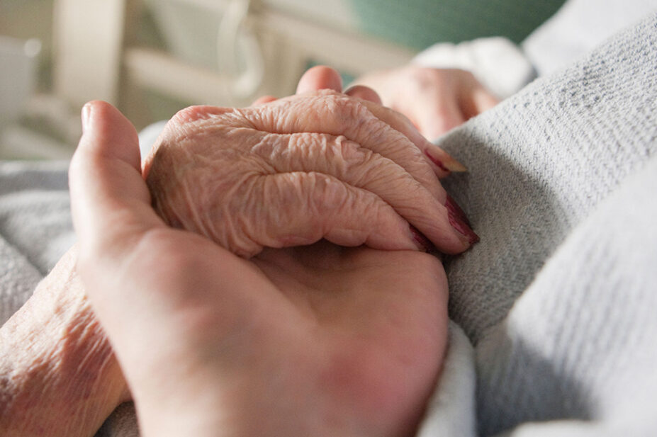 An older person with an IV holds a loved one's hand