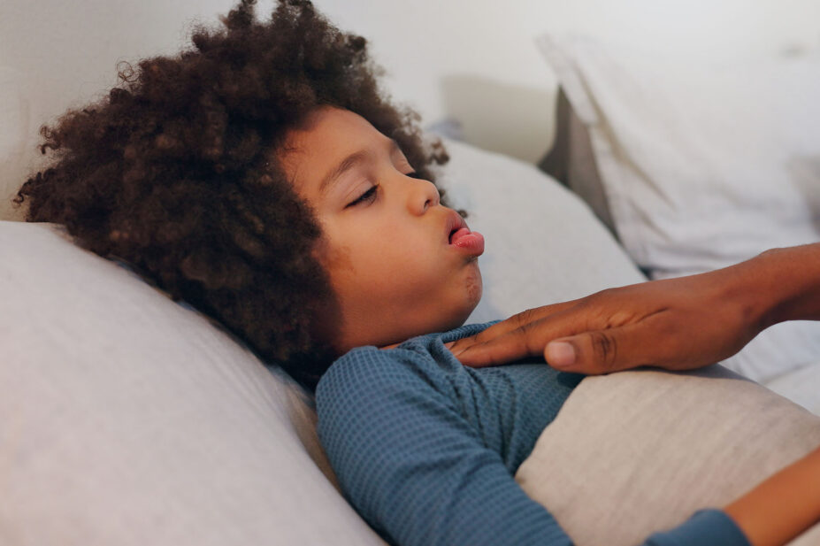 Sick boy coughing in bed and parent resting hand on chest of child