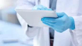 Physician wearing gloves holding a tablet in a laboratory, suggestive of clinical research