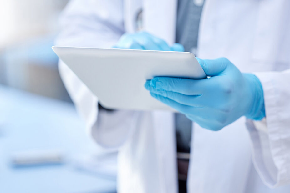 Physician wearing gloves holding a tablet in a laboratory, suggestive of clinical research