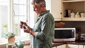 A man holding a bottle of CBD oil in his kitchen