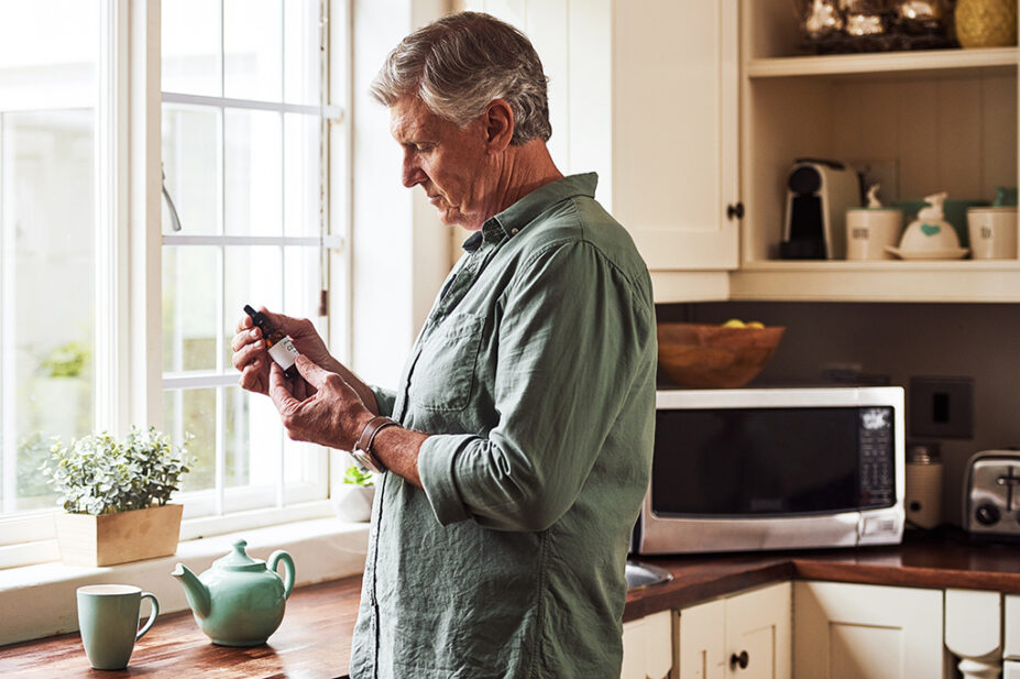 A man holding a bottle of CBD oil in his kitchen