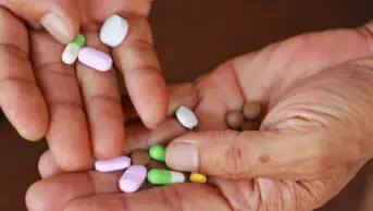 Close up of older person's hands holding several pills and tablets