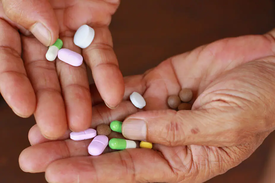 Close up of older person's hands holding several pills and tablets