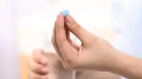 A woman takes a blue pill with a glass of water