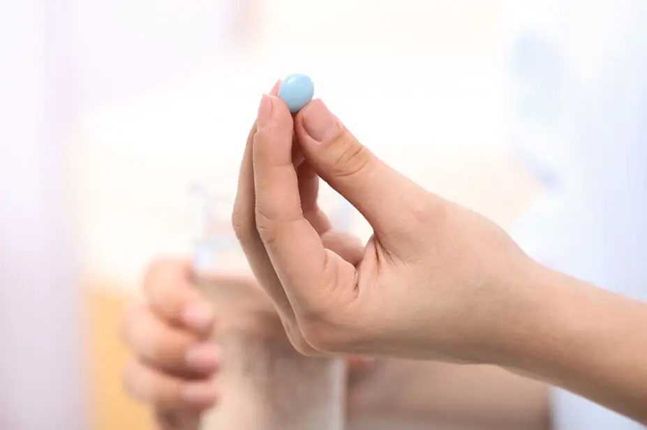 A woman takes a blue pill with a glass of water