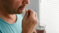 A man takes medication with a glass of water