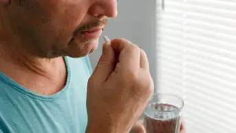 A man takes medication with a glass of water