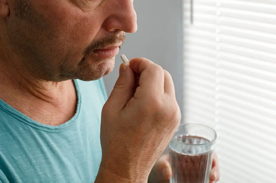 A man takes medication with a glass of water