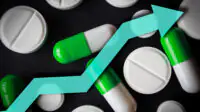 Black background with white pills and green and white tablets and a blue arrow pointing upwards