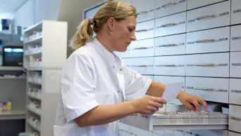 A pharmacist examines the a shelf of medicines