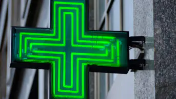 A neon green cross outside of community pharmacy