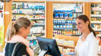 A pharmacist serves a customer in a community pharmacy
