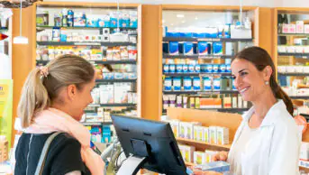 A pharmacist serves a customer in a community pharmacy