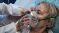Close up of older woman with COVID-19 with oxygen mask on in hospital bed