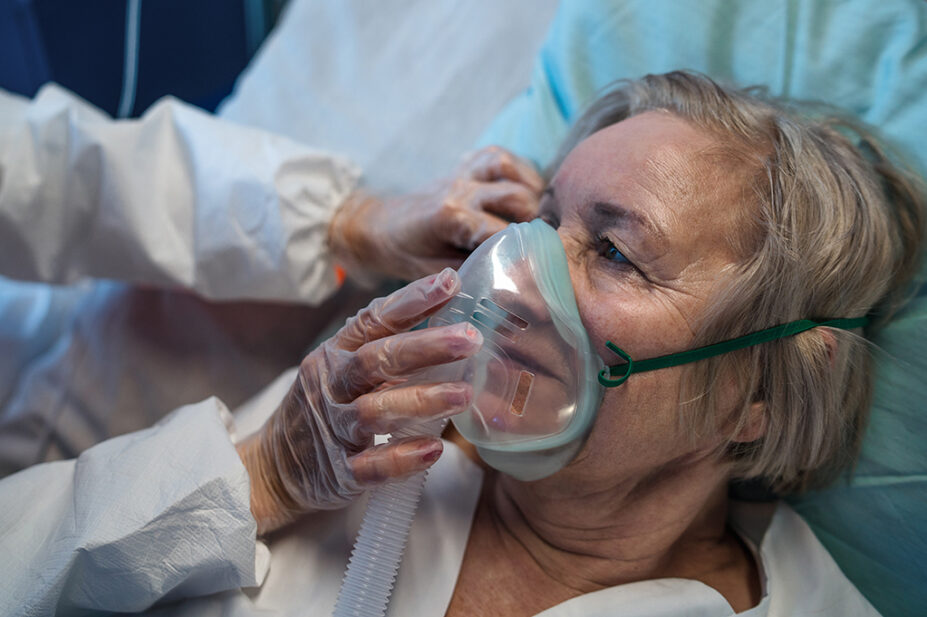 Close up of older woman with COVID-19 with oxygen mask on in hospital bed